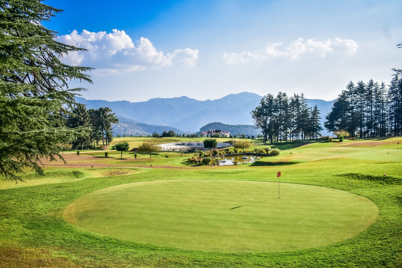 A golf green and fairway set against a forested mountain valley